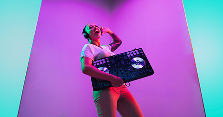 Image showing Young caucasian female musician in headphones performing on purple background in neon light