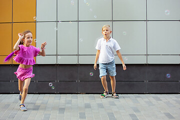 Image showing Two smiling kids, boy and girl running together in town, city in summer day