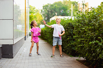 Image showing Two smiling kids, boy and girl running together in town, city in summer day