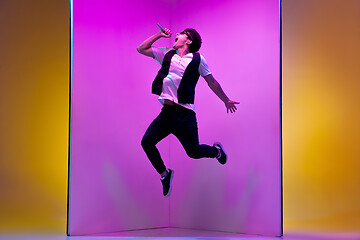 Image showing Young male musician, singer performing on pink-orange background in neon light