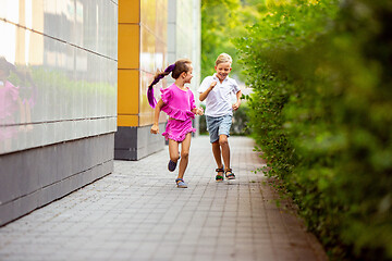 Image showing Two smiling kids, boy and girl running together in town, city in summer day