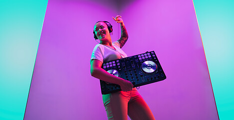 Image showing Young caucasian female musician in headphones performing on purple background in neon light