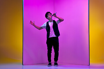 Image showing Young male musician, singer performing on pink-orange background in neon light