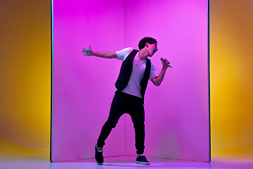 Image showing Young male musician, singer performing on pink-orange background in neon light