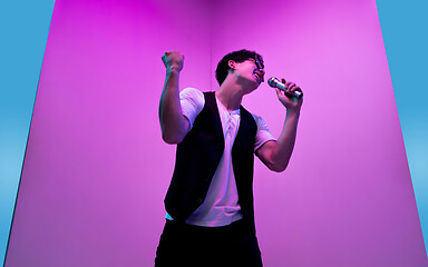 Image showing Young male musician, singer performing on pink-blue background in neon light