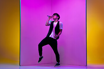 Image showing Young male musician, singer performing on pink-orange background in neon light