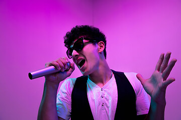 Image showing Young male musician, singer performing on pink background in neon light