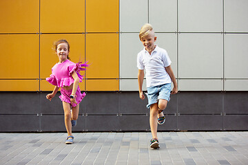 Image showing Two smiling kids, boy and girl running together in town, city in summer day