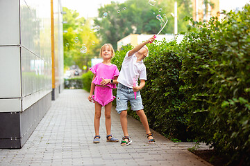 Image showing Two smiling kids, boy and girl running together in town, city in summer day