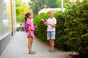 Image showing Two smiling kids, boy and girl running together in town, city in summer day