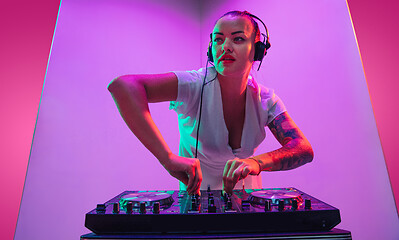 Image showing Young caucasian female musician in headphones performing on purple background in neon light