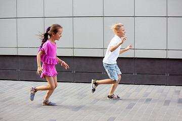 Image showing Two smiling kids, boy and girl running together in town, city in summer day