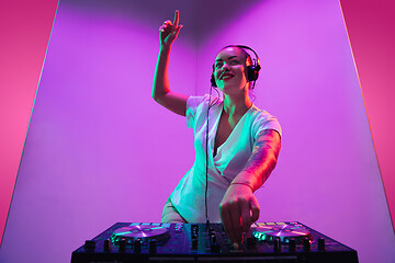 Image showing Young caucasian female musician in headphones performing on purple background in neon light