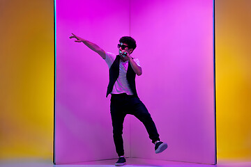 Image showing Young male musician, singer performing on pink-orange background in neon light