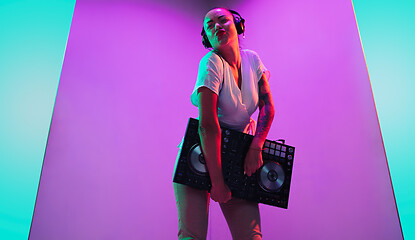 Image showing Young caucasian female musician in headphones performing on purple background in neon light