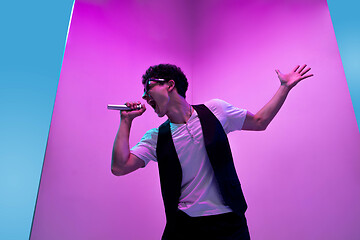 Image showing Young male musician, singer performing on pink-bluebackground in neon light