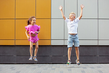 Image showing Two smiling kids, boy and girl running together in town, city in summer day