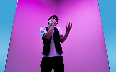 Image showing Young male musician, singer performing on pink-bluebackground in neon light