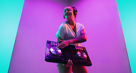 Image showing Young caucasian female musician in headphones performing on purple background in neon light