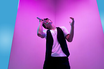 Image showing Young male musician, singer performing on pink-bluebackground in neon light