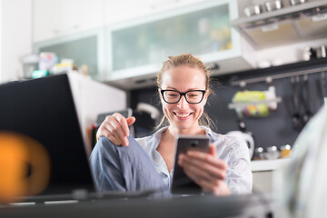 Image showing Stay at home and social distancing. Woman in her casual home clothing working remotly from kitchen dining table. Video chatting using social media with friend, family, business clients or partners