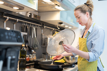 Image showing Stay at home housewife woman cooking in kitchen, stir frying dish in a saucepan, preparing food for family dinner.