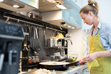 Image showing Stay at home housewife woman cooking in kitchen, stir frying dish in a saucepan, preparing food for family dinner.