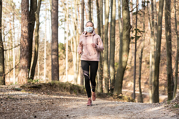Image showing Corona virus, or Covid-19, is spreading all over the world. Portrait of caucasian sporty woman wearing a medical protection face mask while running in nature.