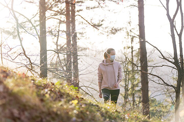 Image showing Corona virus, or Covid-19, is spreading all over the world. Portrait of caucasian sporty woman wearing a medical protection face mask while walking in the forest. Corona virus.