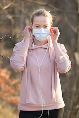 Image showing Portrait of caucasian sporty woman wearing medical protection face mask while walking in park, relaxing and listening to music. Corona virus, or Covid-19, is spreading all over the world