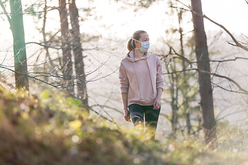 Image showing Corona virus, or Covid-19, is spreading all over the world. Portrait of caucasian sporty woman wearing a medical protection face mask while walking in the forest. Corona virus.