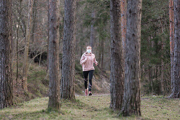 Image showing Corona virus, or Covid-19, is spreading all over the world. Portrait of caucasian sporty woman wearing a medical protection face mask while running in nature.