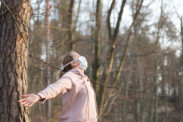 Image showing Portrait of caucasian sporty woman wearing medical protection face mask while relaxing by taking a deep breath in forest. Corona virus, or Covid-19, is spreading all over the world