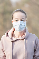 Image showing Portrait of caucasian sporty woman wearing medical protection face mask while walking in park, relaxing and listening to music. Corona virus, or Covid-19, is spreading all over the world