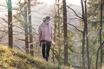 Image showing Corona virus, or Covid-19, is spreading all over the world. Portrait of caucasian sporty woman wearing a medical protection face mask while walking in the forest. Corona virus.