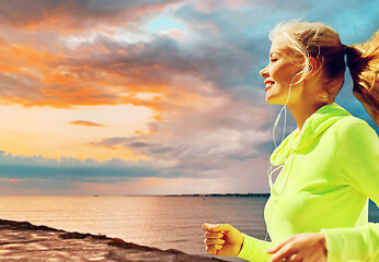 Image showing woman with earphones running over sea sunset