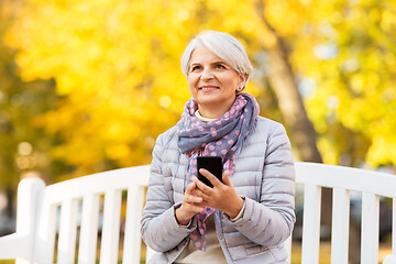 Image showing happy senior woman with smartphone at autumn park