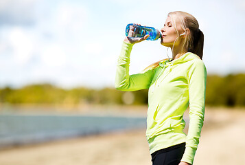 Image showing woman drinking water after exercising on beach