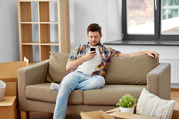 Image showing man with smartphone and boxes on sofa at new home