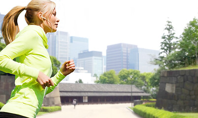 Image showing woman with earphones running at city park