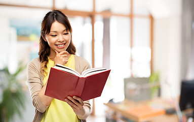 Image showing happy asian woman reading book at office