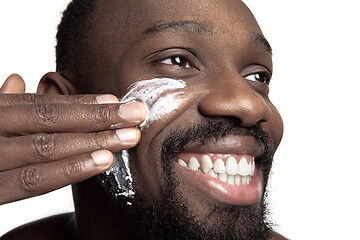 Image showing Young african-american guy applying face cream under his eyes on white background