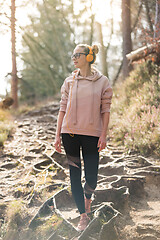 Image showing Active sporty woman listening to the music while hiking in autumn fall forest. Female jogger training outdoor. Healthy lifestyle image of young caucasian woman walking on hiking trail in nature