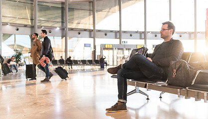 Image showing Casual young male using her cell phone while waiting to board a plane at airport departure gates.