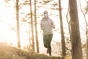 Image showing Corona virus, or Covid-19, is spreading all over the world. Portrait of caucasian sporty woman wearing a medical protection face mask while running in nature.