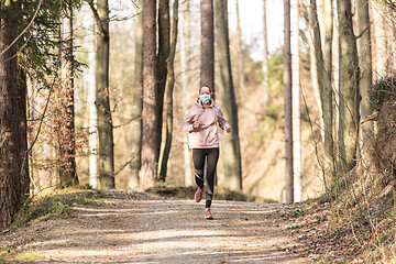 Image showing Corona virus, or Covid-19, is spreading all over the world. Portrait of caucasian sporty woman wearing a medical protection face mask while running in nature.