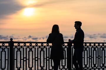 Image showing Two young people are talking while standing at sunset against the backdrop of the sea landscape