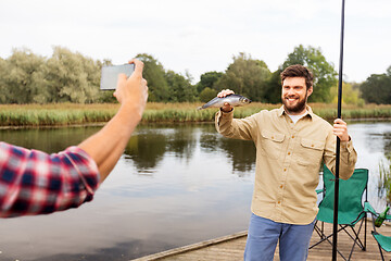 Image showing friend photographing fisherman with fish at lake