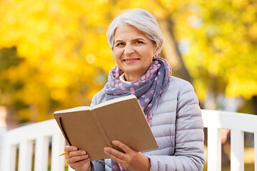 Image showing happy senior woman reading diary at autumn park