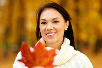 Image showing happy young woman with maple leaf in autumn park